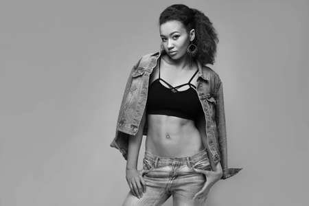 Portrait of glamor elegant black woman model in jeans and jacket posing on a gray background in studioの写真素材