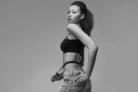 Portrait of glamor elegant black woman model in jeans and stockings posing on a gray background in studioの写真素材