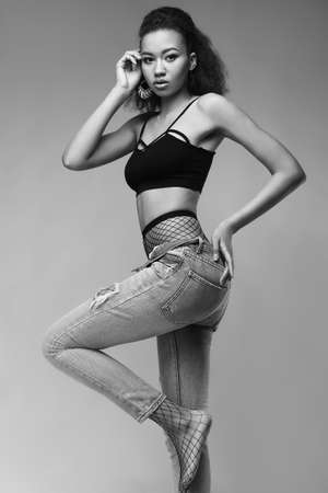 Portrait of glamor elegant black woman model in jeans and stockings posing on a gray background in studioの写真素材