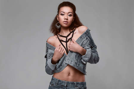 Portrait of glamor elegant black woman model in jeans jacket posing on a gray background in studioの写真素材