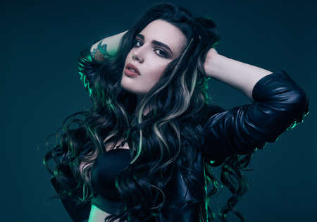Portrait of young sexy girl with long hair in leather jacket on dark background in studioの写真素材