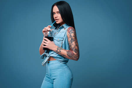 Glamorous fashion portrait of beautiful charming girl with tattoo holding a soda on a bright background in the studioの写真素材