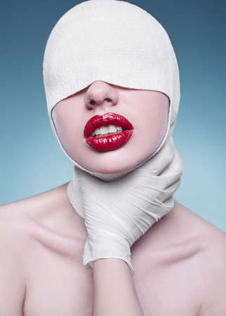 Portrait of young fashion woman with bandaged head and nurse hands on bright backgroundの写真素材