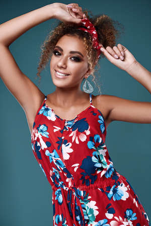 Sensual bright portrait of glamor elegant black woman model with curly hair in red dress posing on colorful background in studioの写真素材