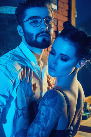 Colorful portrait of beautiful couple: brutal man in elegant suit and sexy girl with a tattoo wearing lingerie in barbershopの写真素材