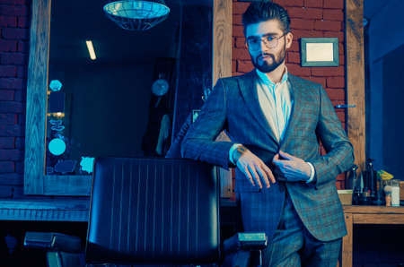 Colorful portrait of brutal man in elegant suit and glasses in barbershopの写真素材