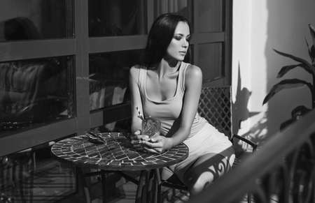 Portrait of a cute and gorgeous latin women in fashion dress sitting on the terrace of the restaurant and drinking cocktailの写真素材