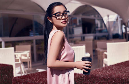 Portrait of a cute and gorgeous asian woman in fashion pink dress posing on terrace of the restaurant with cup of coffeeの写真素材