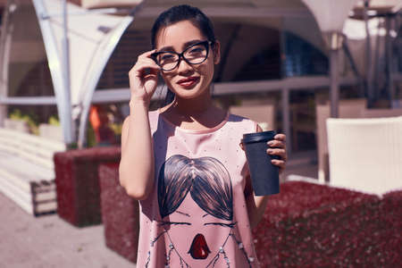 Portrait of a cute and gorgeous asian woman in fashion pink dress posing on terrace of the restaurant with cup of coffeeの写真素材