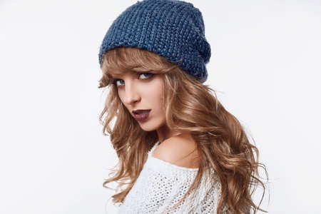 Portrait of sensual positive beautiful blond woman in sweater and blue hat isolated on white background in studioの写真素材