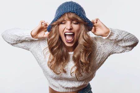 Portrait of sensual smiling beautiful blond woman in sweater and blue hat isolated on white background in studioの写真素材