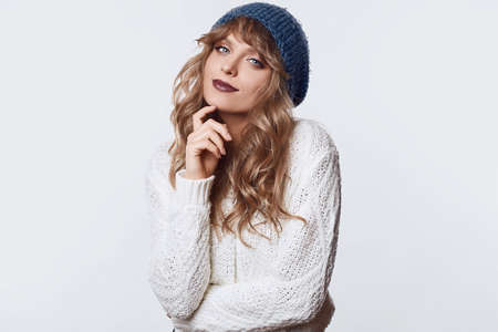 Portrait of sensual positive beautiful blond woman in sweater and blue hat isolated on white background in studioの写真素材