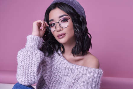 Glamorous fashion portrait of beautiful charming asian girl in purple sweater on bright pink background in studioの写真素材