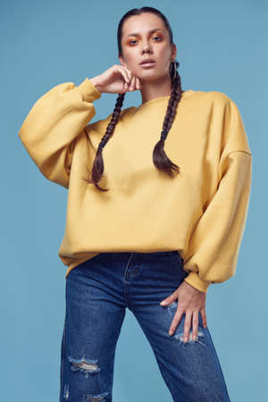 Glamorous fashion portrait of beautiful charming hispanic girl in jeans and yellow hoody on blue...
