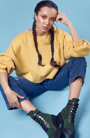 Glamorous fashion portrait of beautiful charming hispanic girl in jeans and yellow hoody on blue...