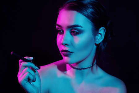 Portrait of glamour seductive gorgeous brunette woman smoking electronic cigarette in neon color...