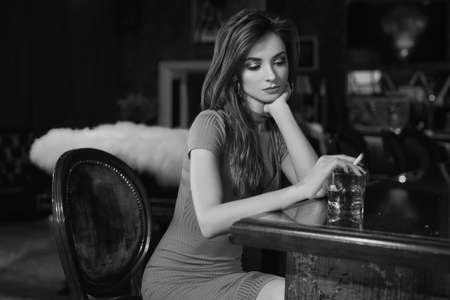 Portrait of gorgeous beauty young brunette woman in red dress sitting at the bar with cigarette and...