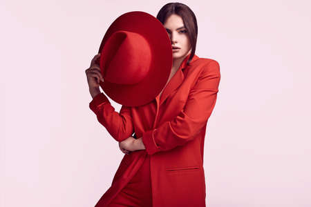 Portrait of elegant beautiful woman in a red fashionable suit and wide hat isolated on white background in studioの写真素材