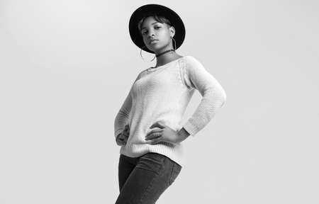 Portrait of young beautiful hipster black girl with short hair in white sweater and fashion hat isolated on white background. Studio shoot.の写真素材