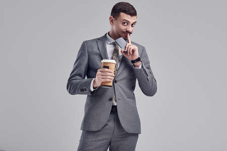 Portrait of handsome young confident arabic businessman with fancy mustache in fashion gray full suit holds a cup of coffee in his hands on studio background.の写真素材