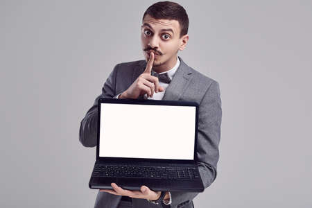 Portrait of handsome young confident arabic businessman with fancy mustache in fashion gray full suit holds black laptop on studio backgroundの写真素材