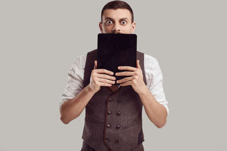 Portrait of handsome young confident arabic businessman with fancy mustache in woolen brown suit holds tablet on studio backgroundの写真素材