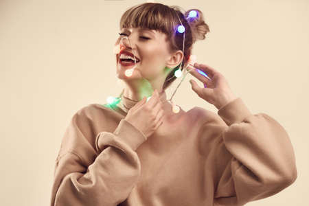 Fashion bright positive portrait of beautiful blond woman with christmas lights on the head. Studio shoot.の写真素材