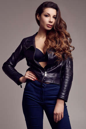 Portrait of young sexy girl with long hair in leather jacket on gray background in studioの写真素材