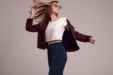 Portrait of cute teenage girl in fashion jacket and color glasses posing on gray background. Studio...