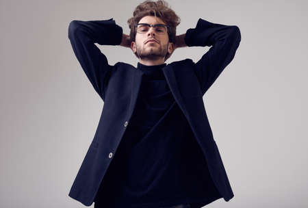 Fashion portrait of handsome elegant man with curly hair wearing suit and glasses on gray background in studioの写真素材