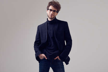 Fashion portrait of handsome elegant man with curly hair wearing suit and glasses on gray background in studioの写真素材