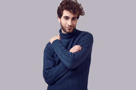 Fashion portrait of handsome elegant man with curly hair in blue sweater isolated on white backgroundの写真素材