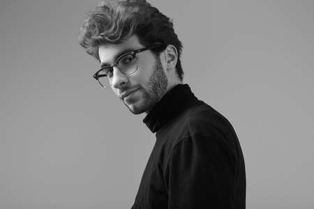 Fashion portrait of handsome elegant man with curly hair wearing black turtleneck and glasses on...