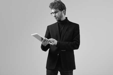 Fashion portrait of handsome elegant man with curly hair wearing suit and glasses holding a tablet...