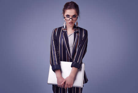 Sensual portrait of elegant glamor woman in fashion suit and glasses with notebook posing on colorful blue background in studioの写真素材