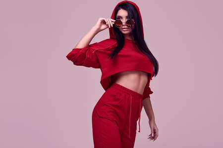 Portrait of gorgeous brunette woman in fashion red hoodie posing on studio background