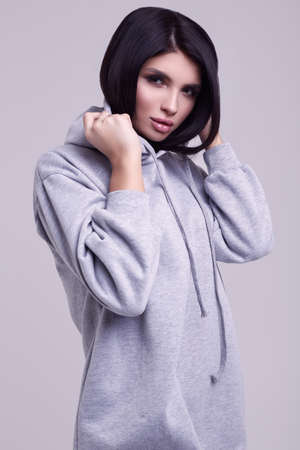 Portrait of gorgeous brunette woman in fashion blue hoodie posing on grey background in studioの写真素材