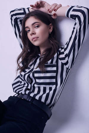 Portrait of fashion brunette woman wearing a striped blouse and jeans isolated on white background in studioの写真素材