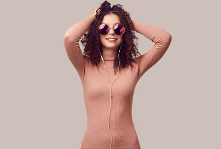 Fashion portrait of bright gorgeous positive girl with curly hair listening music on headphones in...