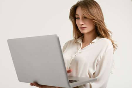 Portrait of gorgeous female brunette model posing in white fashion clothes with laptop in studioの写真素材