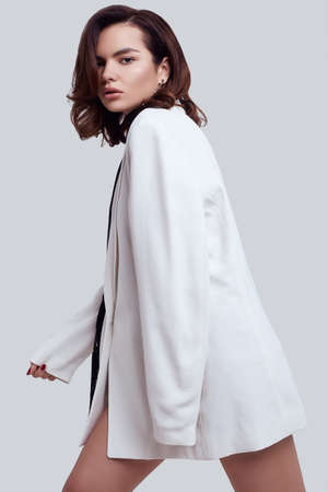 Studio portrait of attractive elegant caucasian woman with dark hair in fashion white suit isolated on light backgroundの写真素材