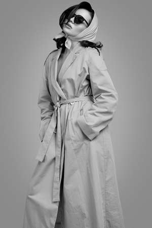 Fashion portrait of young elegant brunette woman in coat and shawl posing on bright background in studioの写真素材