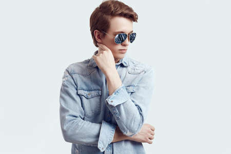 Portrait of handsome hipster man in fashion sunglasses wearing jeans jacket on white background in studioの写真素材