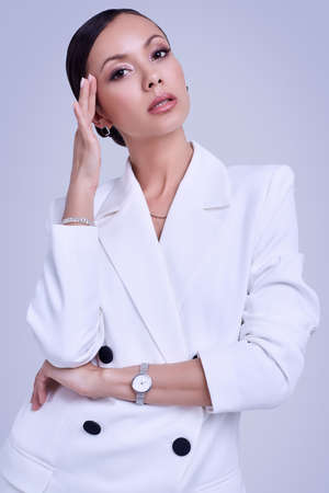 Portrait of a cute and gorgeous latin women in fashion white suit posing on bright studio backgroundの写真素材