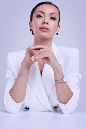 Portrait of a cute and gorgeous latin women in fashion white suit wearing expensive jewelry posing on bright studio backgroundの写真素材