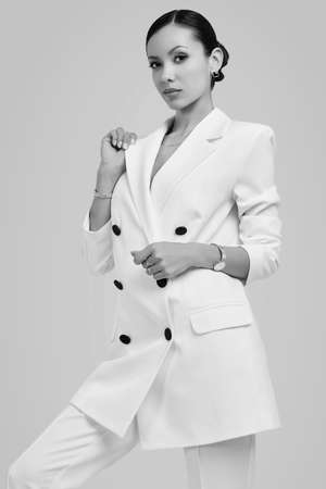 Portrait of a cute and gorgeous latin women in fashion white suit posing on bright studio backgroundの写真素材