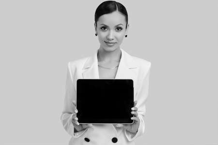 Portrait of a cute and gorgeous latin women in fashion white suit with digital tablet posing on bright studio backgroundの写真素材