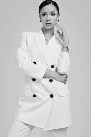 Portrait of a cute and gorgeous latin women in fashion white suit posing on bright studio backgroundの写真素材