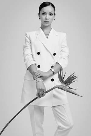 Portrait of a cute and gorgeous latin women in fashion white suit with exotic flower posing on bright studio backgroundの写真素材