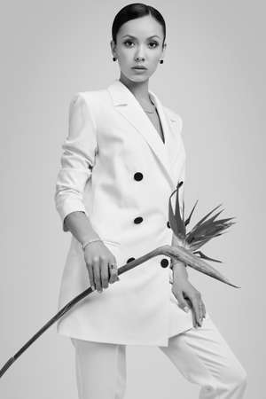 Portrait of a cute and gorgeous latin women in fashion white suit with exotic flower posing on bright studio backgroundの写真素材